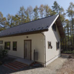 木々に囲まれた白い外壁の平屋住宅の外観